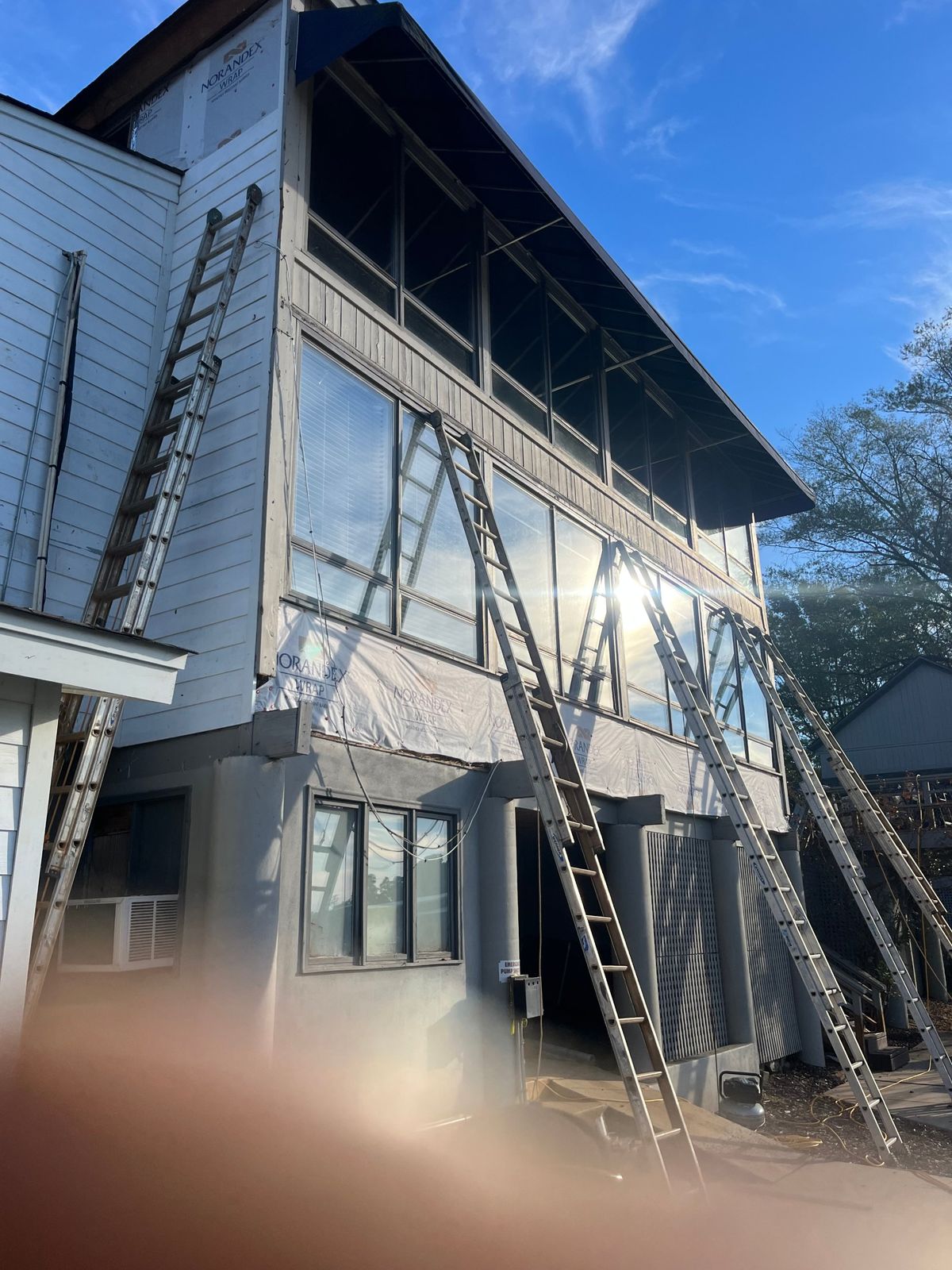 Three-story home wrapped in house wrap with ladders set up during siding replacement